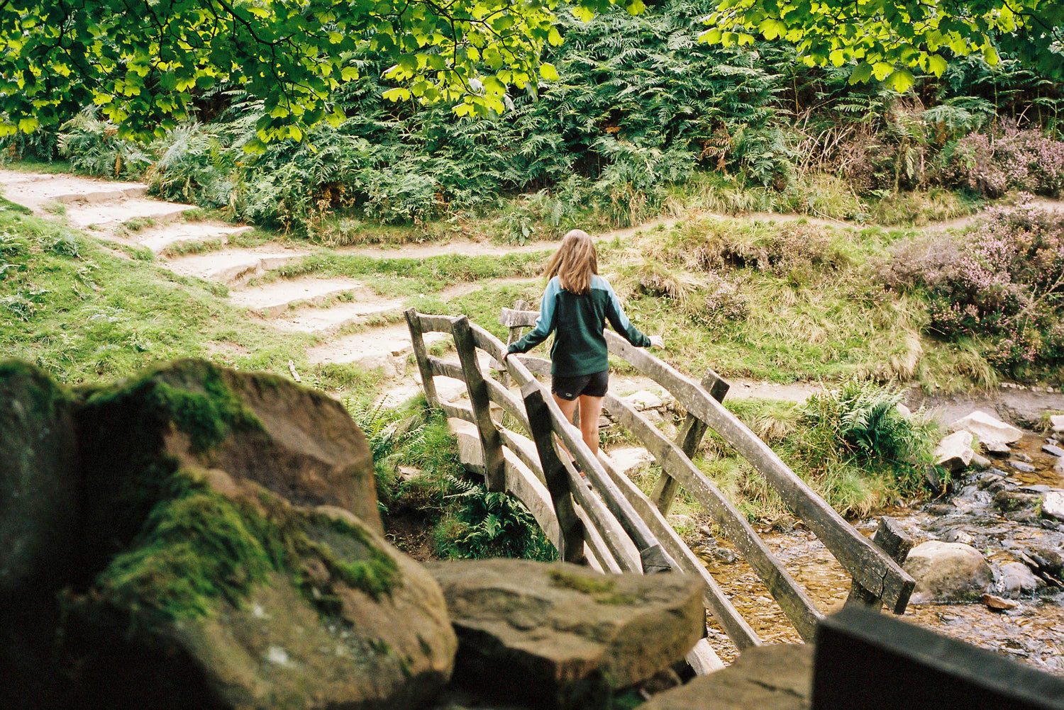 woman crossing wooden bridge over stream on a sunny day